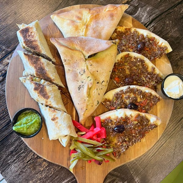 A wooden board with Shawarma Time's Mediterranean platter, including wraps, meat pies, and dips.