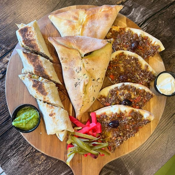 A wooden board with Shawarma Time's Mediterranean food, including wraps, meat pies, and dips.