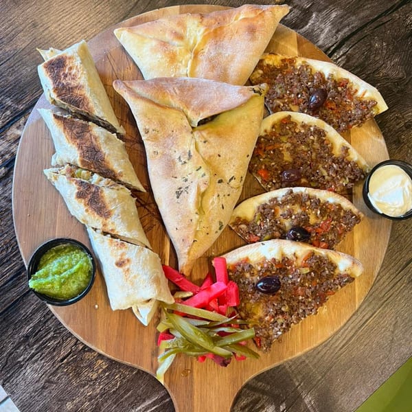 Shawarma Time's Mediterranean platter with wraps, meat pies, and spinach pies on a wooden board.
