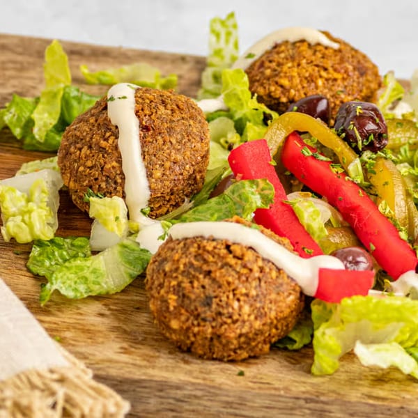 Three falafel balls drizzled with white sauce, served on lettuce with pickled vegetables and olives.